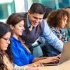 Hispanic professor helping student in busy college classroom