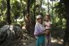 smiling Indian woman with young child in her arms standing near jungle trees